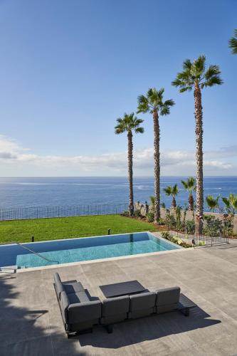 a swimming pool with palm trees and the ocean at La Villa at The Cliff Bay - PortoBay in Funchal