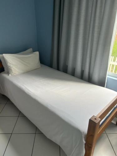 a bed with white sheets and a window with a curtain at 205 Laguna lacrete in Uvongo Beach