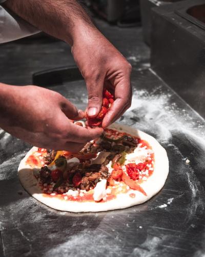 a person adding toppings to a pizza on a counter at The Khyber Himalayan Resort & Spa in Gulmarg