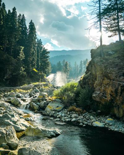 a river with rocks and trees in the background at The Khyber Himalayan Resort & Spa in Gulmarg