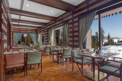 a dining room with tables and chairs and windows at The Khyber Himalayan Resort & Spa in Gulmarg