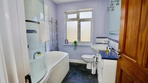 a bathroom with a tub and a toilet and a sink at E2M Stays Beautiful House Close To Heathrow Airport- Walking Distance To Thames River in Egham