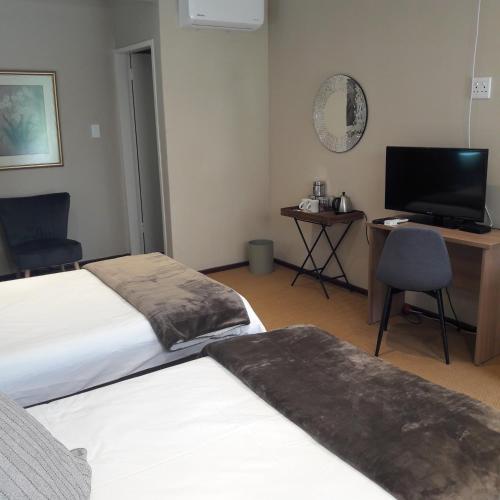 a hotel room with two beds and a desk and a television at Whispering Pines Country Estate in Magaliesburg