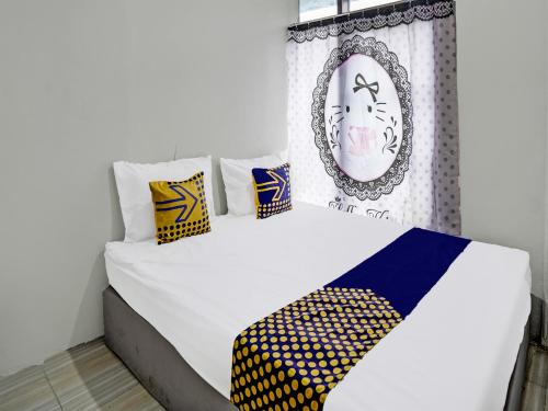een wit bed met gele en blauwe kussens en een spiegel bij SPOT ON 92388 Villa Segi Delapan in Prigen