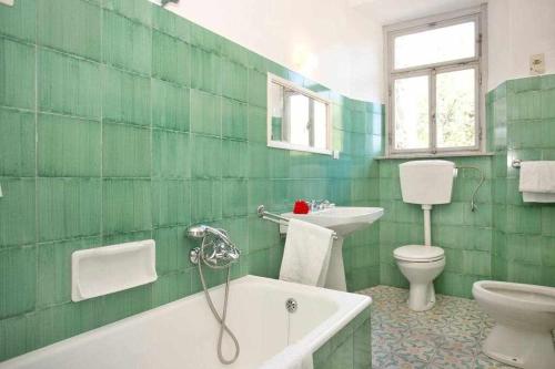 a green tiled bathroom with a tub and a toilet at Villa Trenta Prestigious Villa Enchanting Garden in Lucca