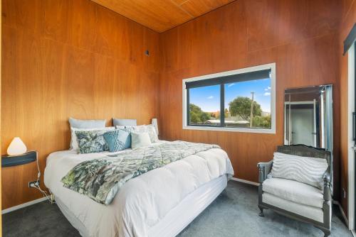 a bedroom with a bed and a window and a chair at Beachside Sanctuary - Otaki Beach Holiday Home in Otaki Beach