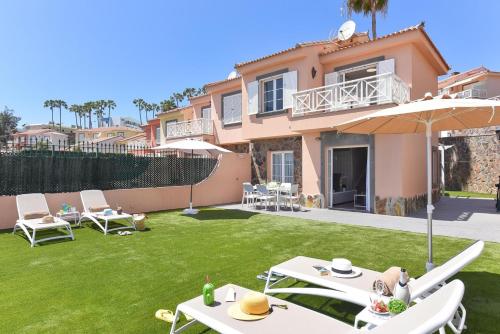 a house with a lawn with white tables and an umbrella at Chalet Santa Ana 25 by VillaGranCanaria in Playa del Ingles