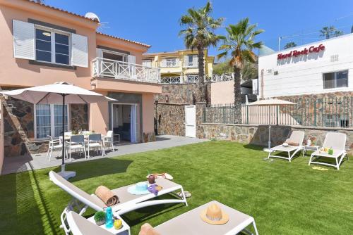 a backyard with a lawn with chairs and tables at Chalet Santa Ana 25 by VillaGranCanaria in Playa del Ingles