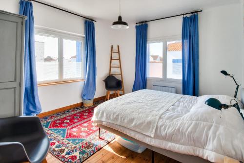een slaapkamer met een bed en blauwe gordijnen en een stoel bij Jolie maison pour 6 a Noirmoutier-en-l Ile in Noirmoutier-en-l'lle
