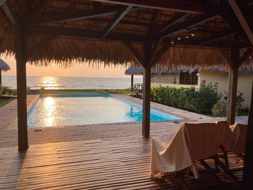 a swimming pool with a straw umbrella and the ocean at La Parenthèse in Nosy Be