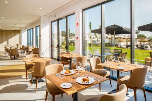 a restaurant with tables and chairs and large windows at AP Cabanas Beach & Nature - Adults Friendly in Cabanas de Tavira