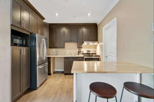 a kitchen with wooden cabinets and a kitchen island with two chairs at INITIAL - CITADIN - Chutes-Montmorency in Boischâtel