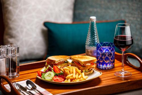 a sandwich and french fries on a table with a glass of wine at Holiday Inn Manchester Airport T2 by IHG in Hale