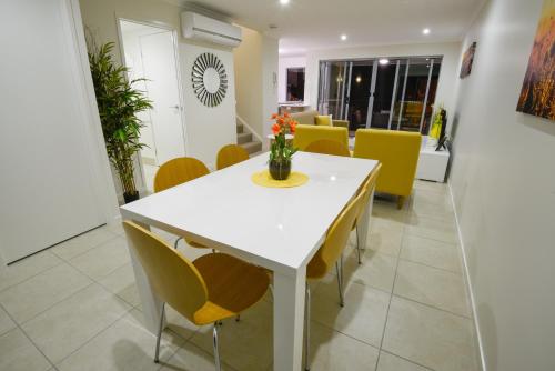 a dining room with a white table and yellow chairs at Direct Collective - Breeze on Brightwater in Mooloolaba