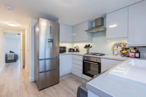a kitchen with white cabinets and a stainless steel refrigerator at Central Windsor Modern Garden Flat, Walk 2 Sights - By Tempstay in Windsor