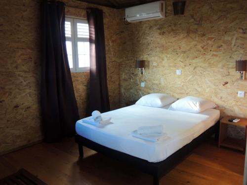 um quarto com uma cama com lençóis brancos e uma janela em Chalet d'une chambre avec piscine partagee jardin et wifi a Bouillante a 1 km de la plage em Bouillante