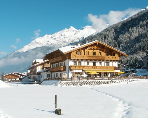 een groot houten gebouw in de sneeuw met bergen bij Hotel Brunnenhof in Neustift im Stubaital