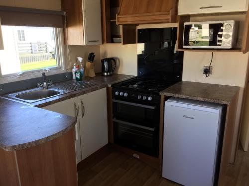a small kitchen with a stove and a sink at Beside the Seaside, Pakefield Holiday Park, Arbor Lane, Pakefield, Lowestoft NR33 7BE in Pakefield