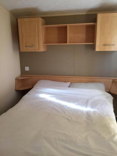 1 dormitorio con 1 cama blanca y armarios de madera en Beside the Seaside, Pakefield Holiday Park, Arbor Lane, Pakefield, Lowestoft NR33 7BE, en Pakefield