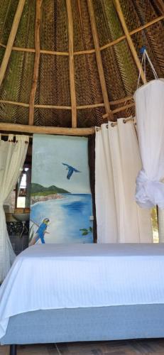 1 dormitorio con 1 cama con cortinas y una pintura en Hostal Zirumake Dentro del Parque Tayrona, en El Zaino