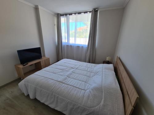 sypialnia z białym łóżkiem i telewizorem w obiekcie Comodo y acogedor departamento w mieście Puerto Montt