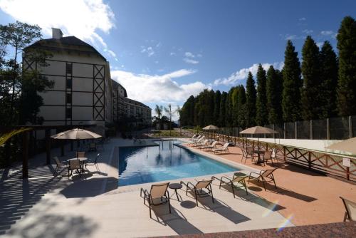 uma piscina com cadeiras e guarda-sóis ao lado de um edifício em Vista Azul Apart Hotel - Vista Pedra Azul com Cozinha Compacta em Domingos Martins