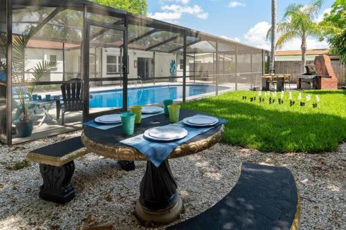 a table with plates on it next to a pool at Tranquil Times a Serene 3BR Close to RJ Stadium with Screened Heated Pool, Outdoor Kitchen and Yard Chess in Tampa