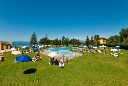 um grupo de pessoas sentadas ao redor de uma piscina com guarda-sóis em Campeggio del Garda em Peschiera del Garda