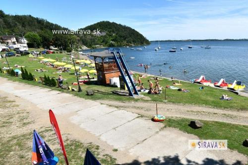 a group of people sitting on the grass by the water at Apartmán Bling s vírivkou Zemplínska Šírava in Kaluža