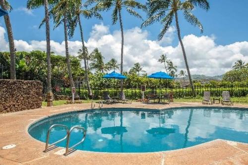 una piscina con palmeras y sombrillas azules en Kauai Makanui by Coldwell Banker Island Vacations, en Koloa