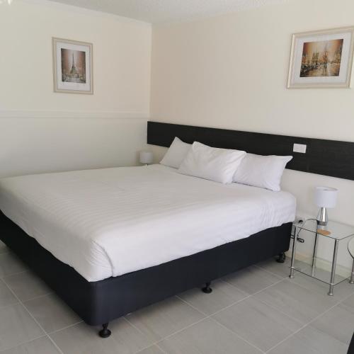 a bedroom with a large bed with white sheets at Gallery Motel in Murwillumbah