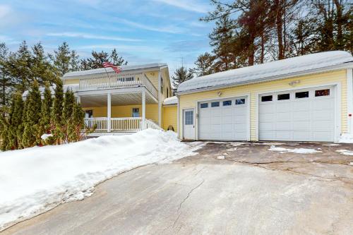 a yellow house with two garage doors in the snow at Cherry Valley Retreat in Gilford