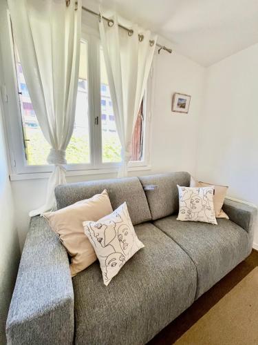 - un canapé gris avec des oreillers en face d'une fenêtre dans l'établissement Studio les pieds dans l'eau, à Deauville