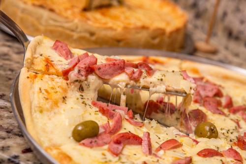 a slice of pizza with ham and olives on a pan at Pousada Vila Barequeçaba in São Sebastião