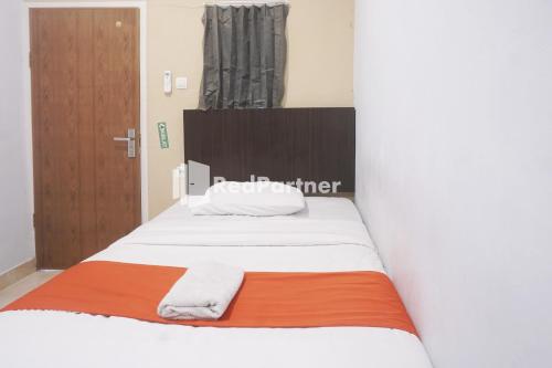 a bedroom with a bed with white sheets and an orange blanket at Tassa Homestay Syariah Mitra RedDoorz in Jambi