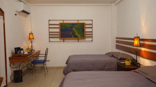汕埠的住宿－Hotel Casa del Arbol，一间卧室配有两张床和一张书桌,墙上挂有绘画作品