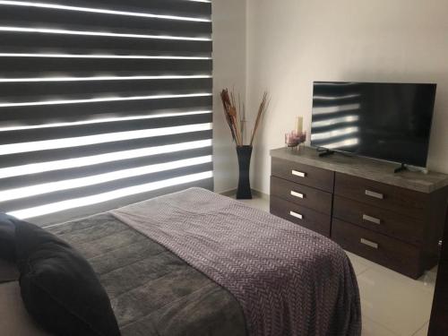 a bedroom with a bed and a dresser with a flat screen tv at Acogedora y amplia casa, alberca climatizada previa reserva in Juriquilla