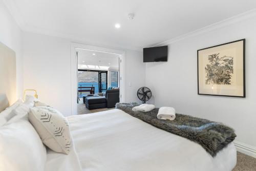 a white bedroom with a large white bed and a living room at Beacon Lakeside Luxury 908 - 3 Bedroom in Queenstown