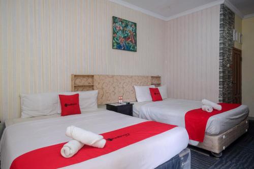 RedDoorz at Mamagayo Inn Yogyakarta في يوغياكارتا: غرفة فندقية بسريرين بملاءات حمراء وبيضاء