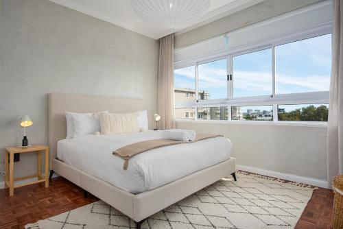 Dormitorio blanco con cama y ventana grande en Doric Court 605, en Ciudad del Cabo