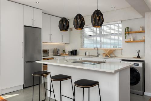 una cocina con armarios blancos y una barra con taburetes en Doric Court 605, en Ciudad del Cabo