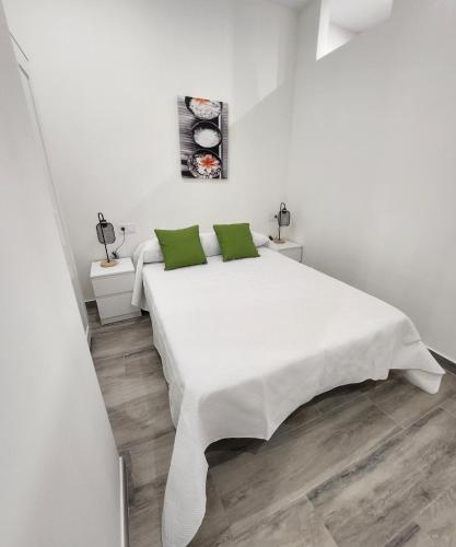 a white bedroom with a large white bed with green pillows at Green Apartamentos Cartagena in Cartagena
