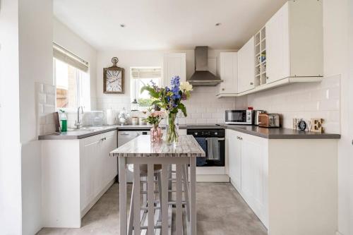 a kitchen with white cabinets and a table with flowers on it at Stevenage Contractors x8 New 3 bedroom House Free Wifi, Parking, Towels all inclusive & Large Garden in Stevenage
