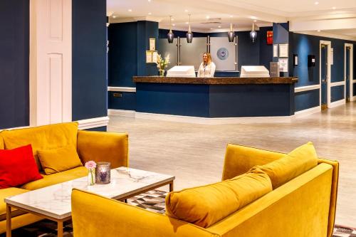 a lobby with yellow couches and a woman standing at a counter at Mercure Swansea Hotel in Swansea