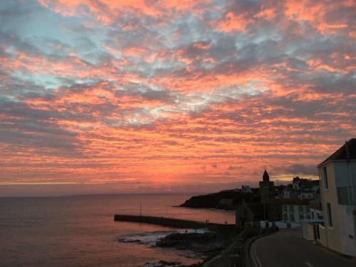 a sunset over the ocean with a pier and buildings at The Old Stores, Luxury beach side selfcatered holiday cottage above the beach in Porthleven