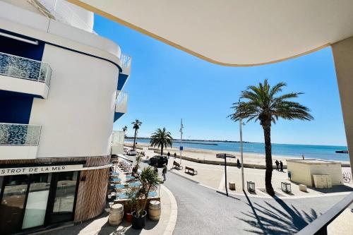 Blick auf den Strand von einem Gebäude mit einer Palme in der Unterkunft Villa Marie 1 - Superbe appartement climatisé 2 chambres Vue Mer in Le Grau-du-Roi