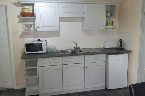 a kitchen with white cabinets and a sink and a microwave at A quiet self-contained flat close to Exeter. in Stoke Canon