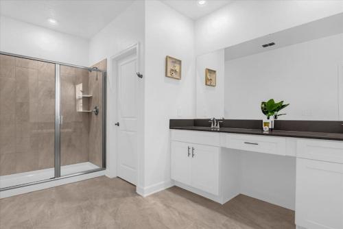 a white bathroom with a shower and a sink at Stylish Resort Villa w Pool Near Disney Gated 5BR in Kissimmee