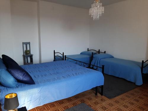 1 Schlafzimmer mit 3 Betten mit blauer Bettwäsche und einem Kronleuchter in der Unterkunft CASA FRIDA in Canelli