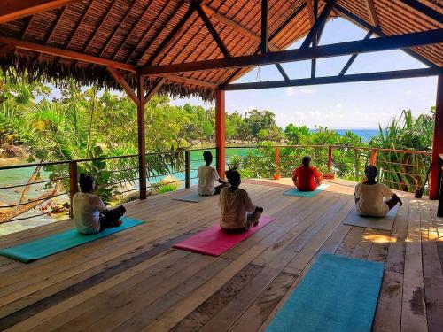 eine Gruppe von Leuten, die auf einem Deck sitzen und Yoga machen in der Unterkunft Natiora Green Lodge in Sainte Marie